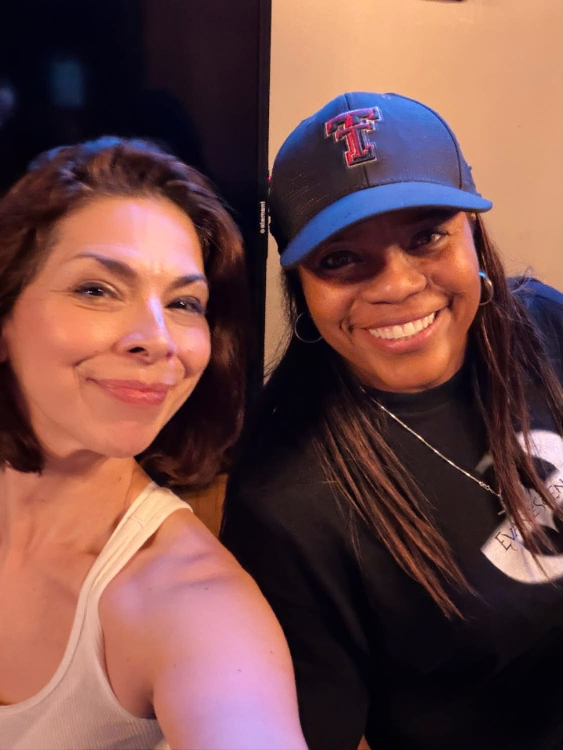 Two women smiling, one with shoulder-length brown hair and the other with long dark hair wearing a Texas Tech cap.