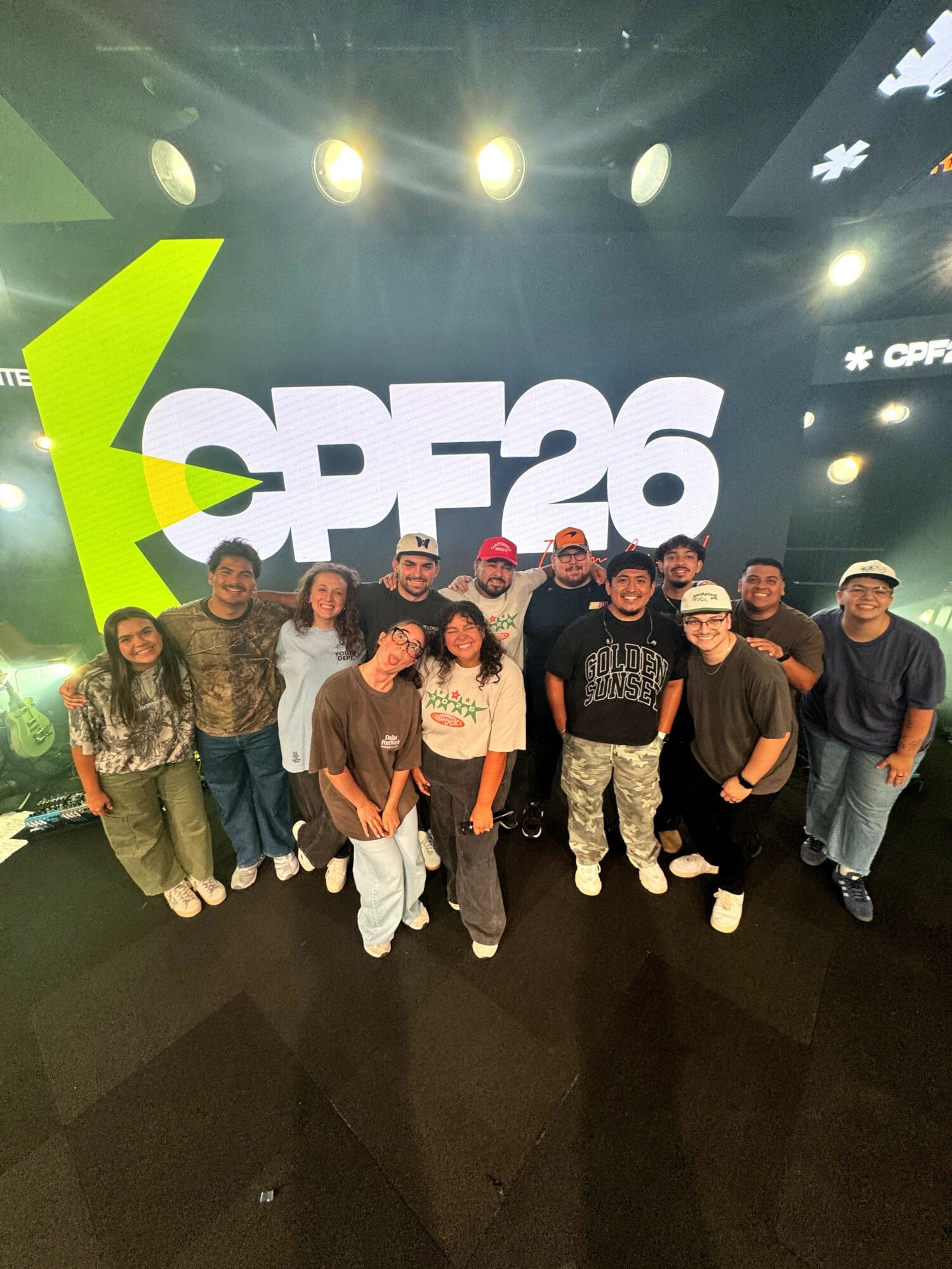 Group of people standing in front of a large screen displaying 'CP26' at an event, with stage lights overhead.