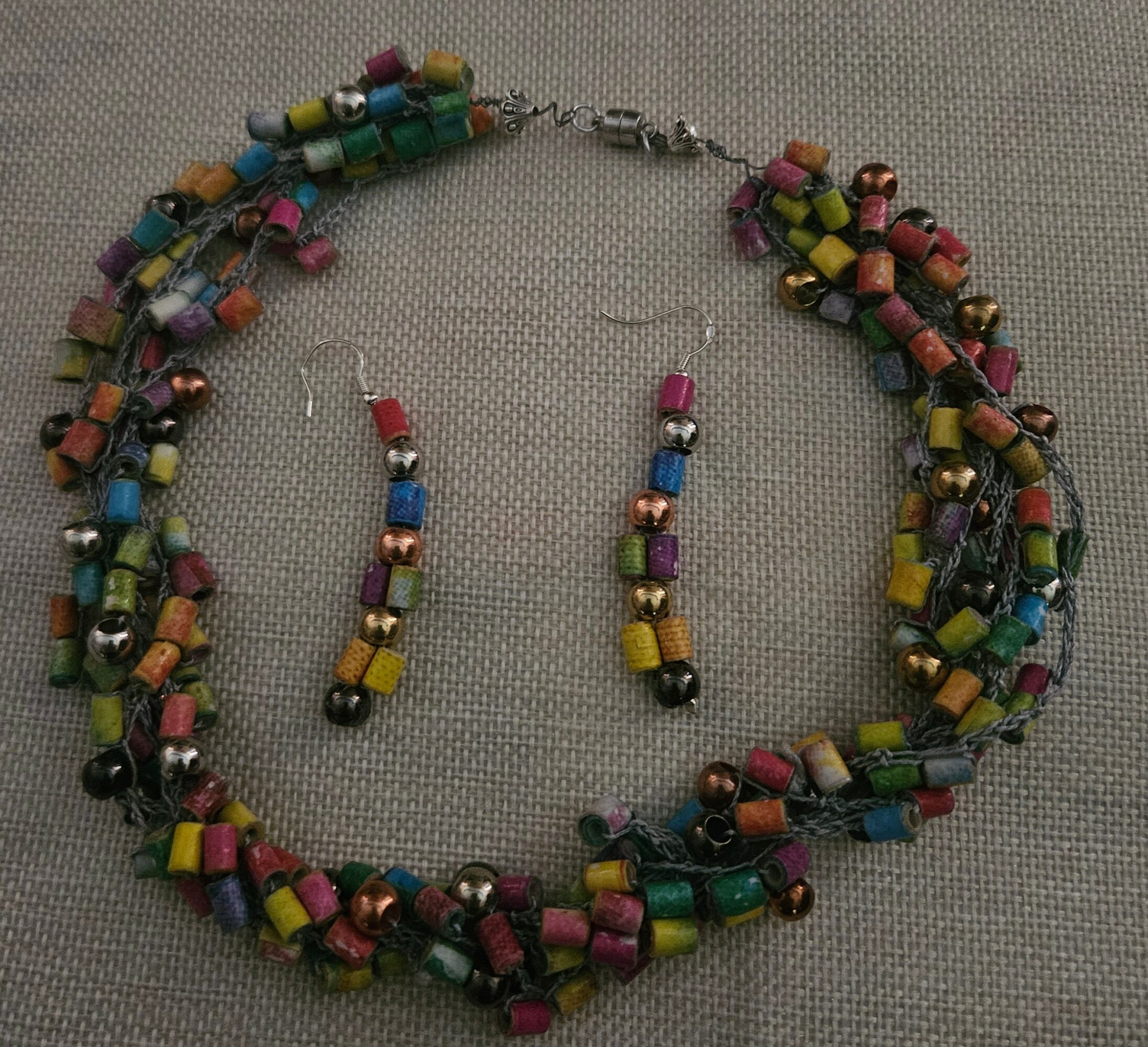 Colorful beaded necklace with multiple strands and a silver clasp, laid on a gray fabric background.