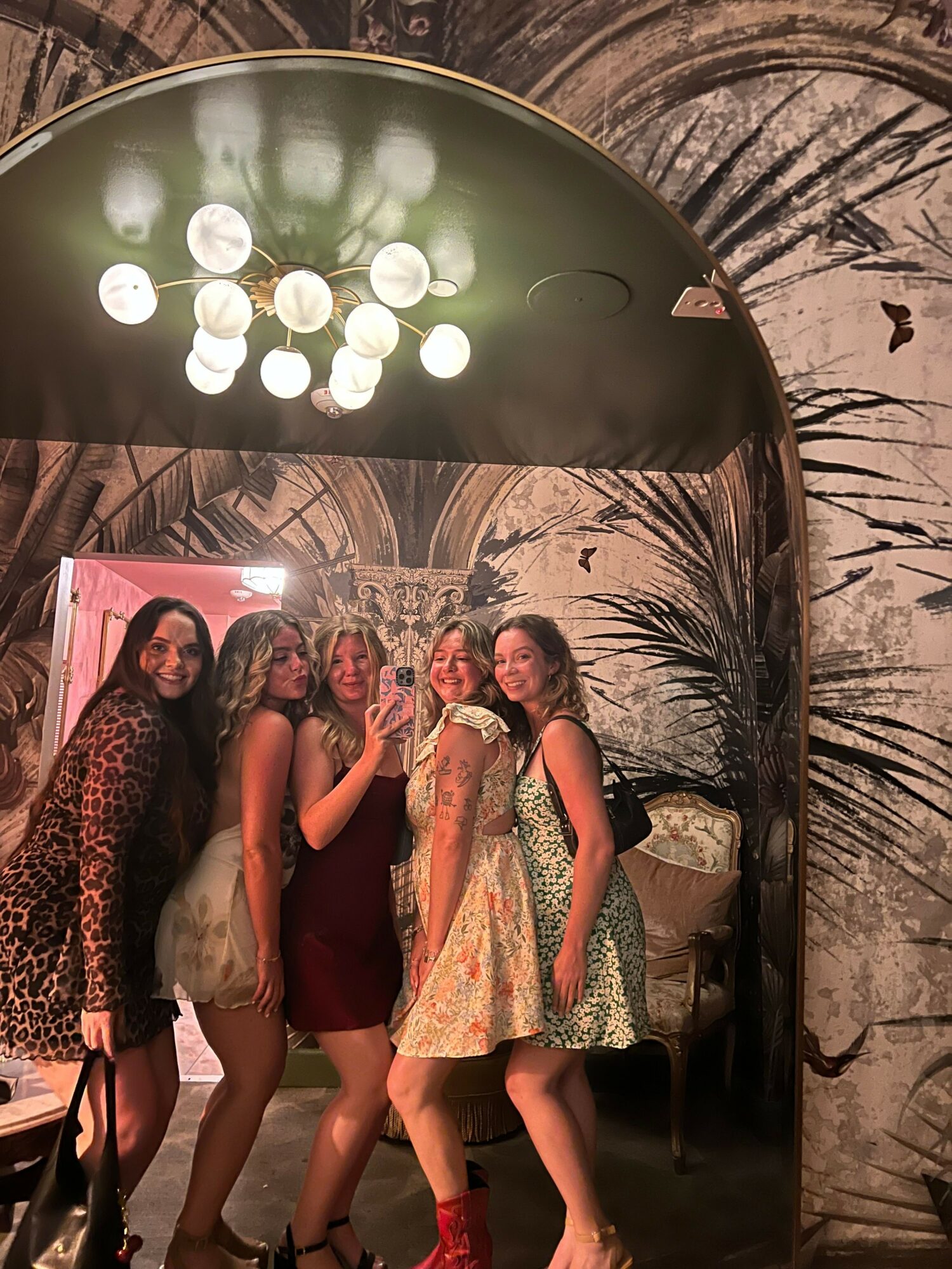 Four women stand together in front of a painted backdrop with hanging lights overhead, posing for a photo.
