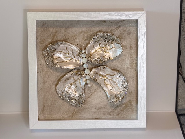 Decorative framed artwork featuring a butterfly with textured, metallic wings and a row of white beads in the center.