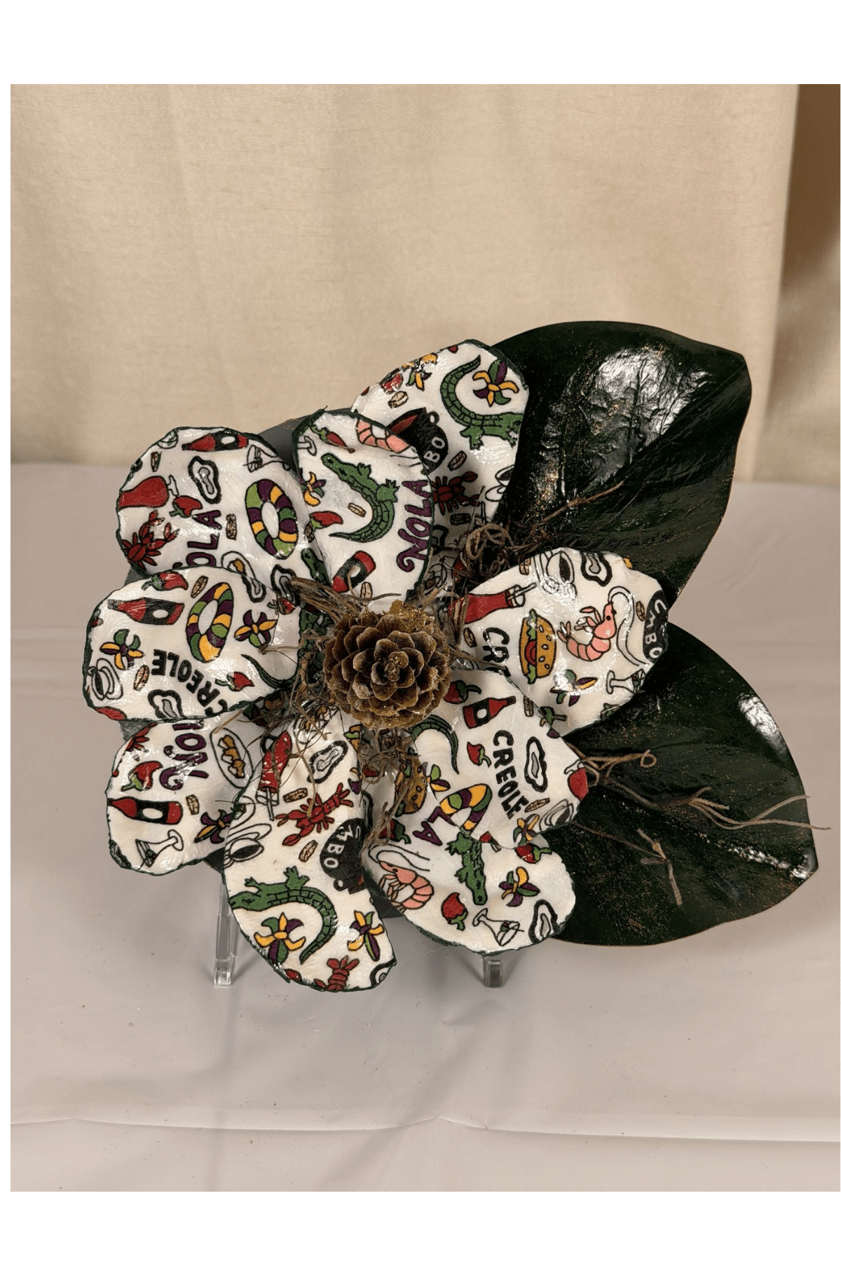 Decorative flower with patterned petals, a pine cone center, and dark green leaves on a light background.
