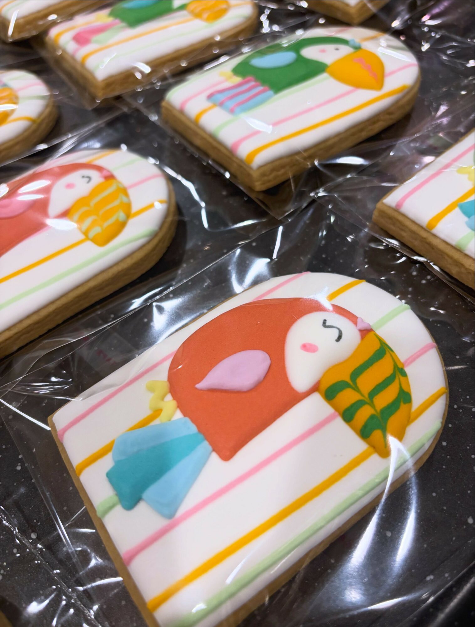Decorated cookies with animal and holiday designs on striped backgrounds, wrapped in clear plastic, arranged on a surface.