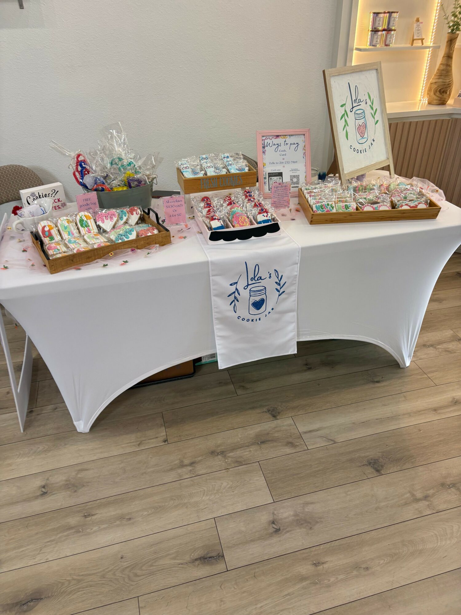 Table with decorative items, framed artwork, and gift bags, set on a wooden floor in a bright room.
