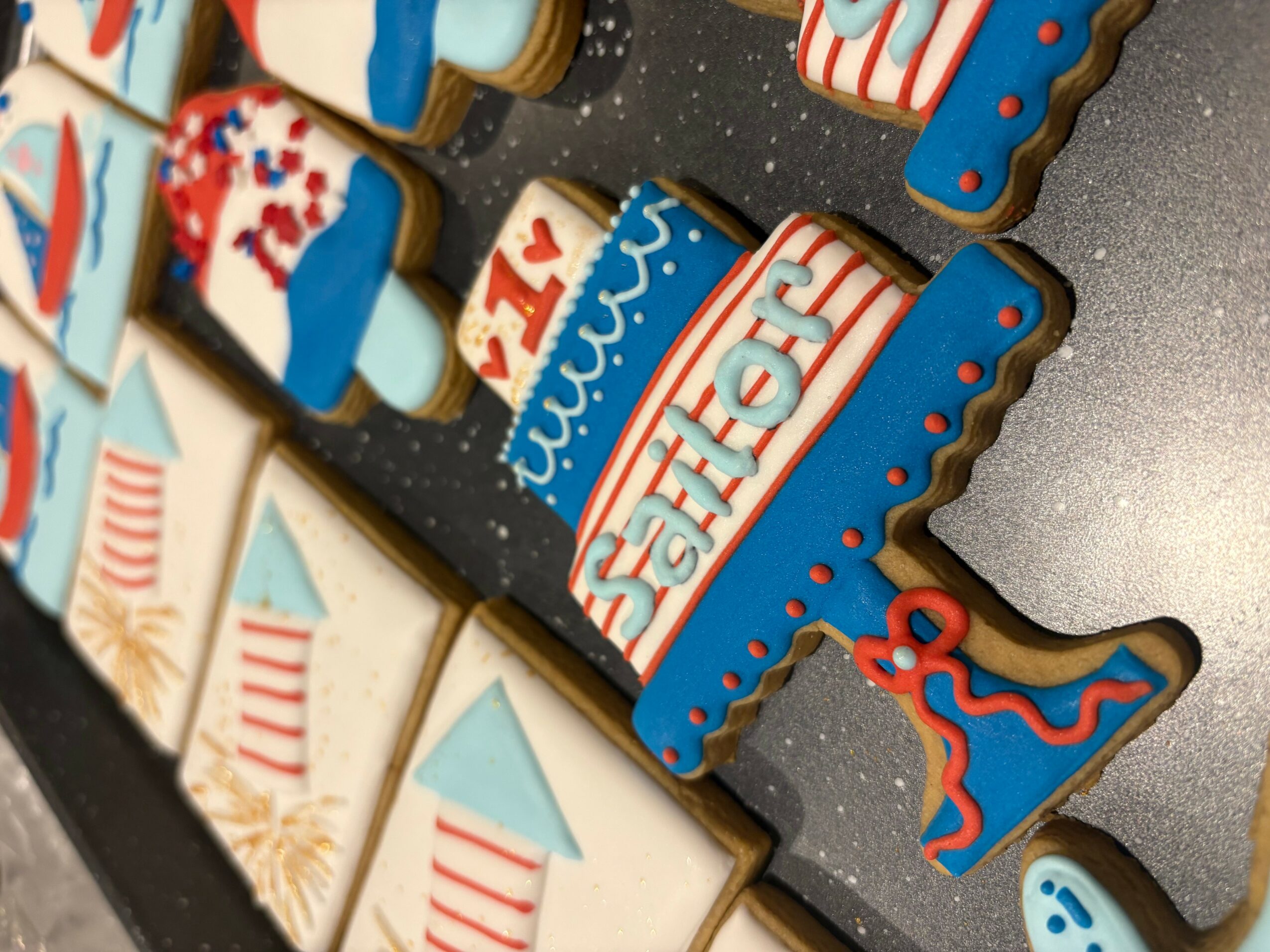 Decorative cookies with patriotic and nautical themes, including flags, sailboats, and the word 'SEAFOR' on a dark surface.