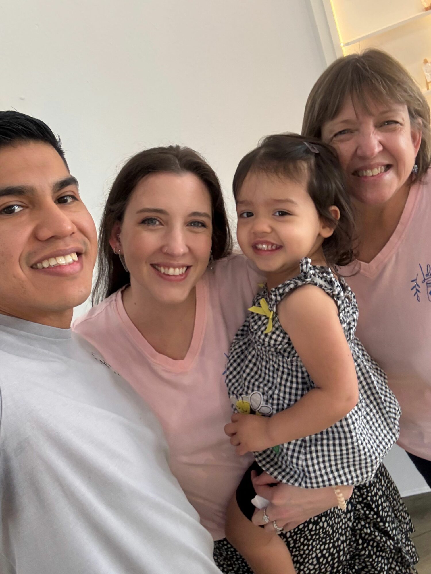 Four smiling people, two adults and two children, pose together indoors, close-up shot, all looking at the camera.