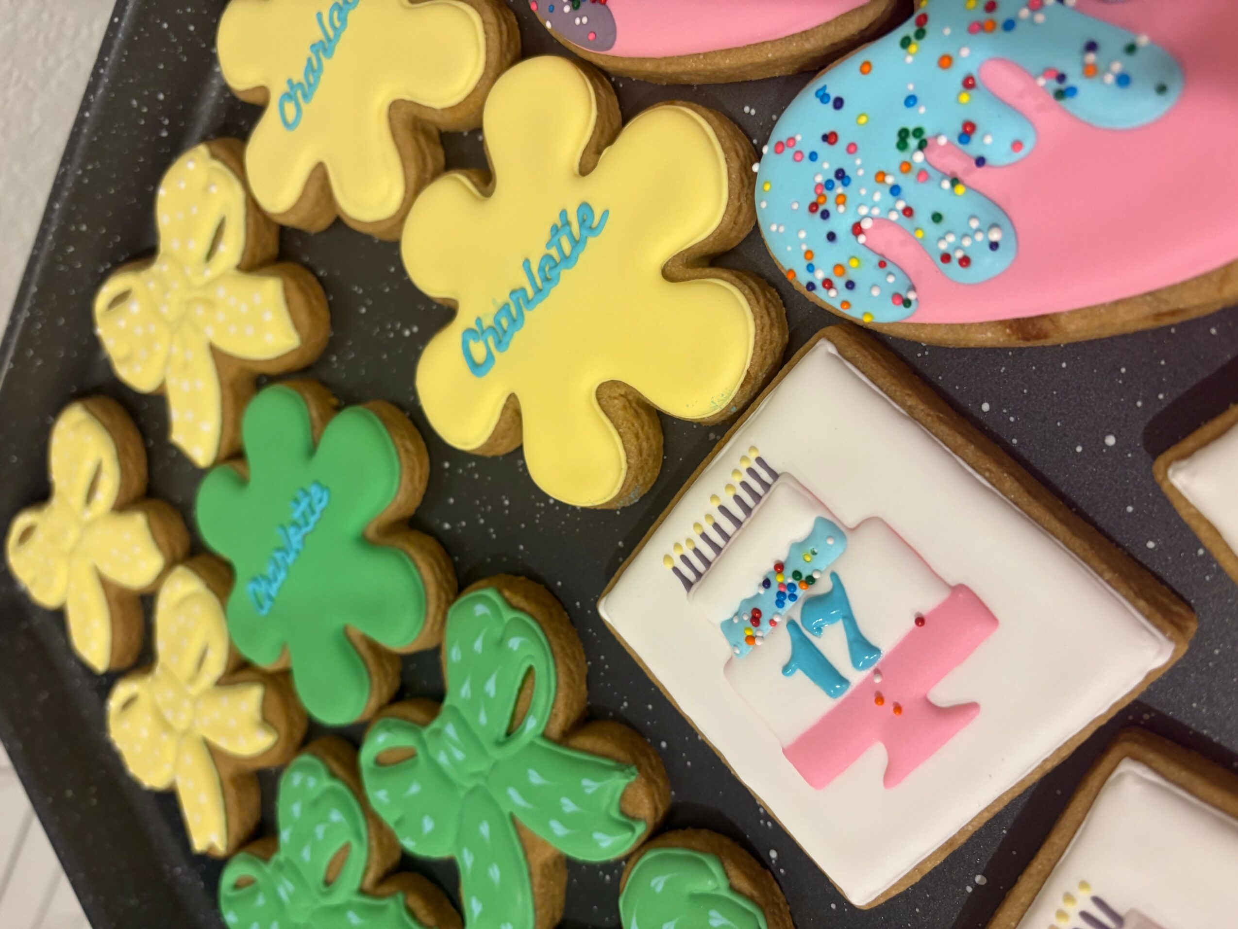 Assorted decorated cookies, including shamrocks, a unicorn, and a pink and blue design, on a black surface.