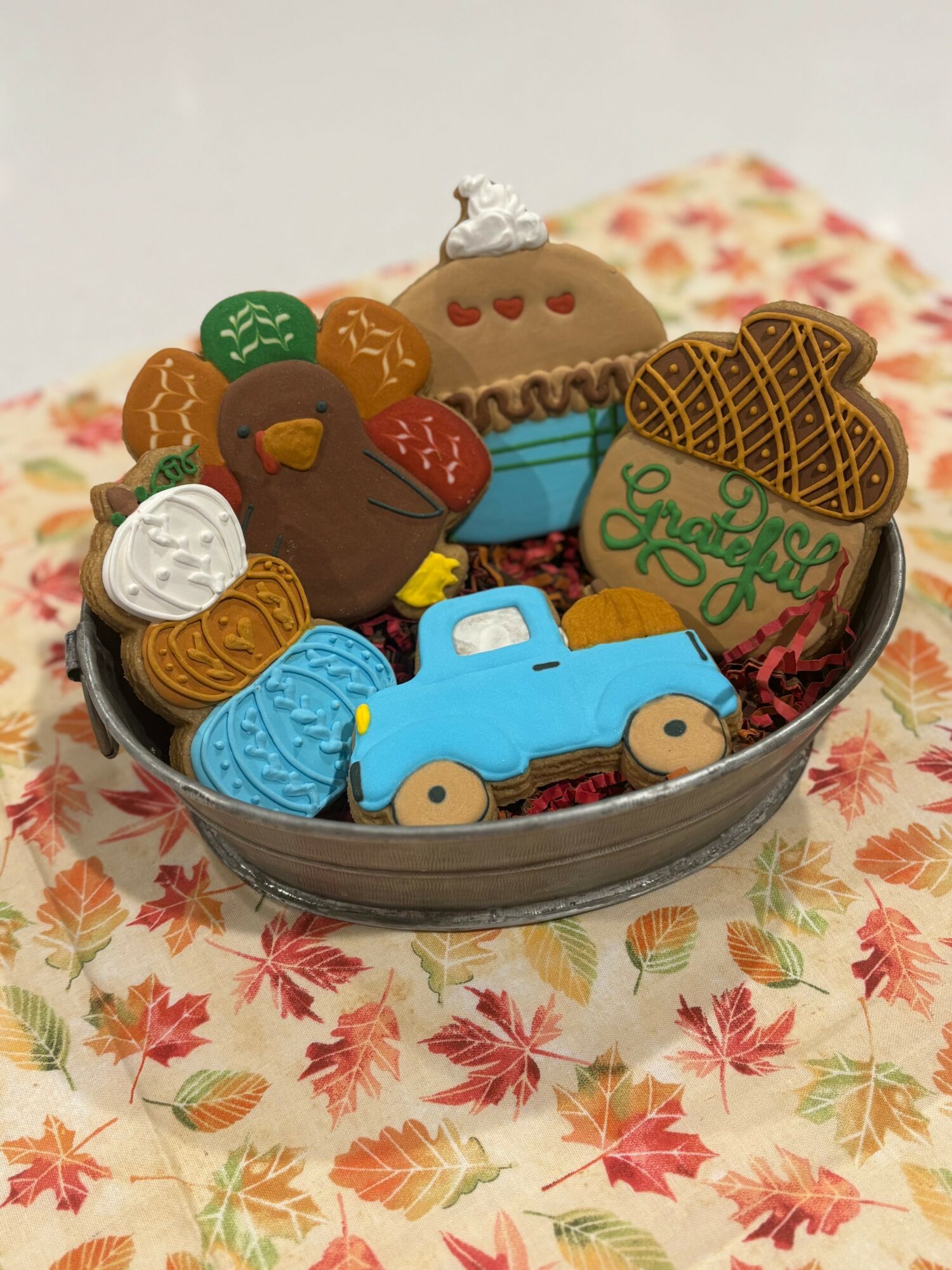 Assorted decorated cookies in a bowl on a floral tablecloth, including a blue car, a cupcake, and various shapes.