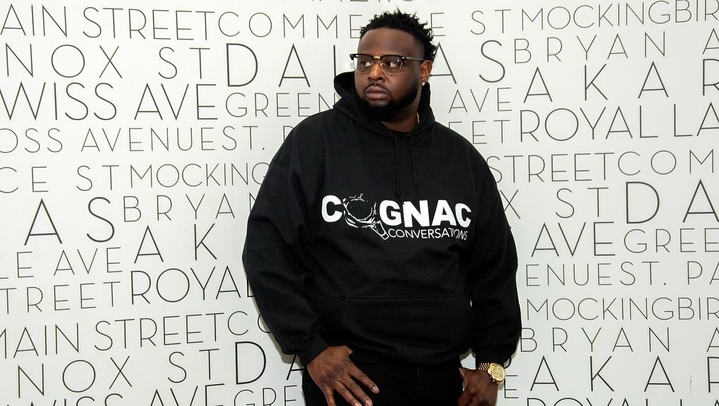 Man with glasses and beard wearing a black hoodie with white text, standing in front of a white background with black text.
