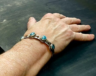 Hand with a bracelet featuring blue stones resting on a dark surface.