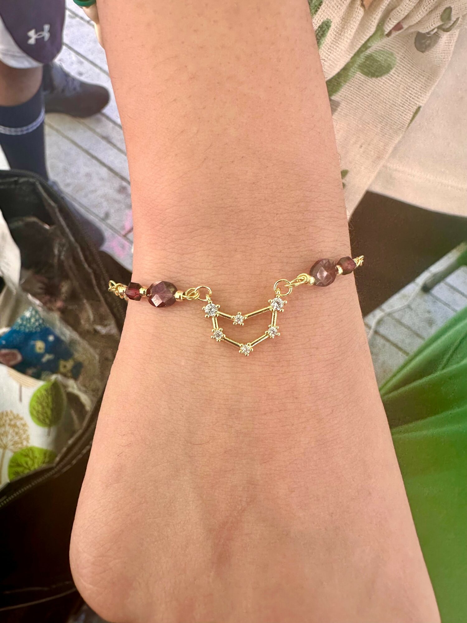 Person's wrist with a beaded bracelet featuring gold and purple beads, and a constellation-shaped charm.