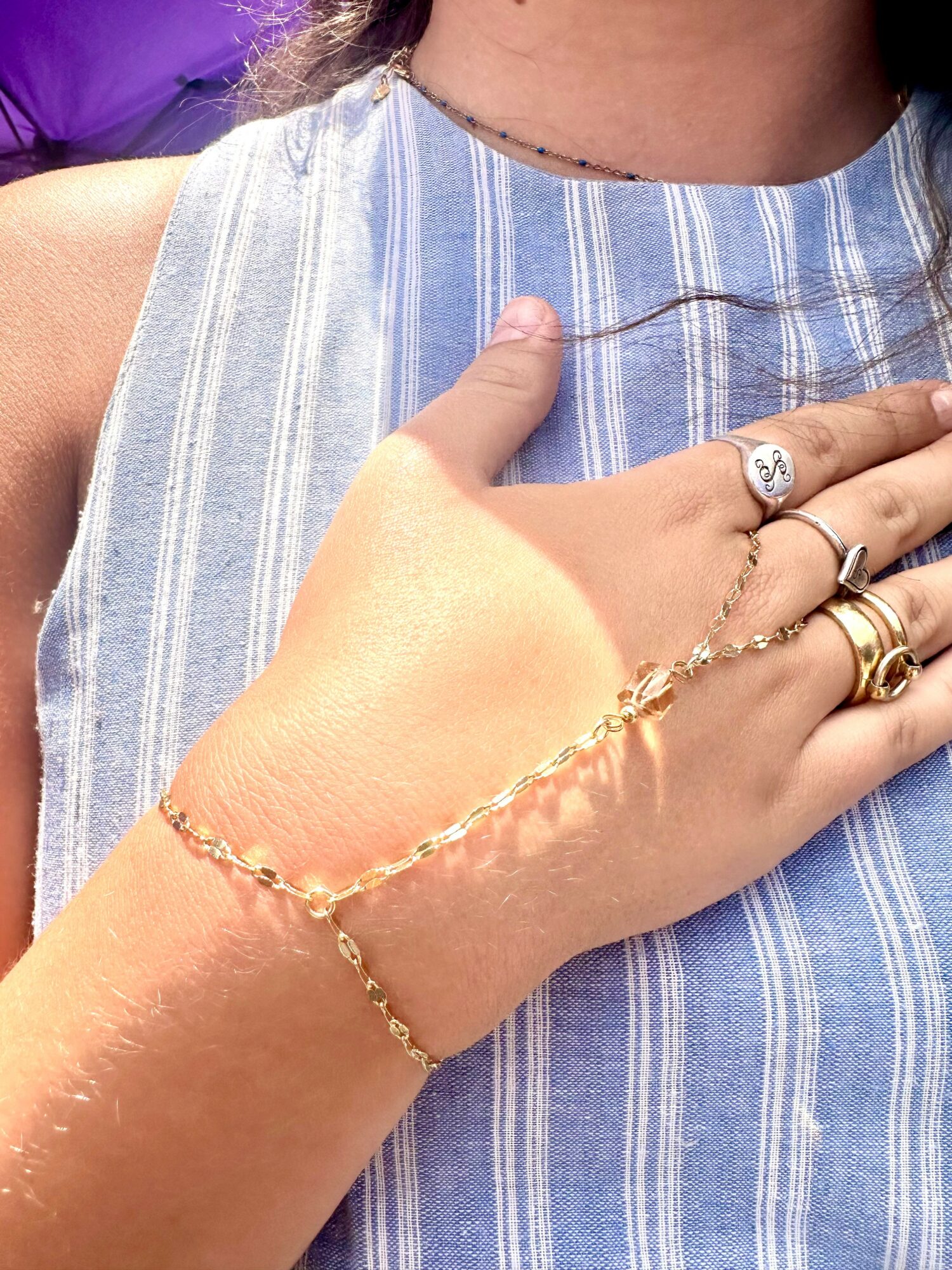 Close-up of a person's hand with rings and a bracelet, resting on their chest in a blue striped sleeveless top.