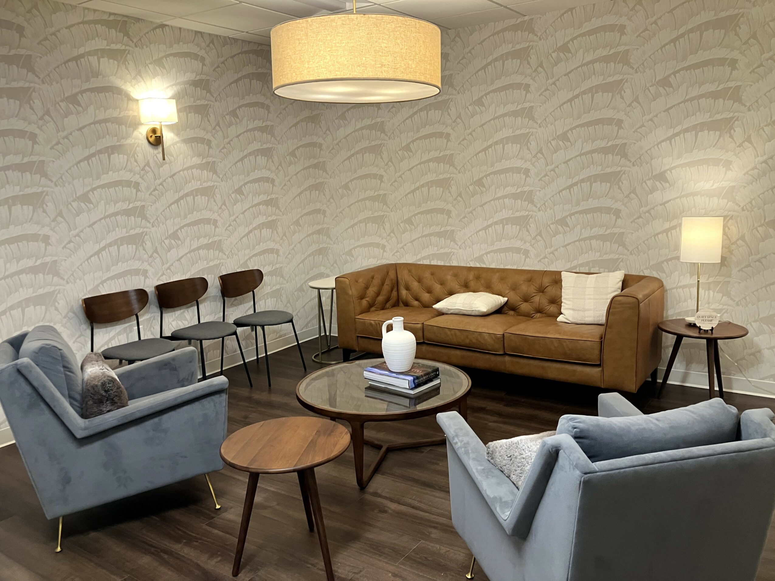 Living room with a brown sofa, two gray armchairs, a round coffee table, and wall-mounted lights.