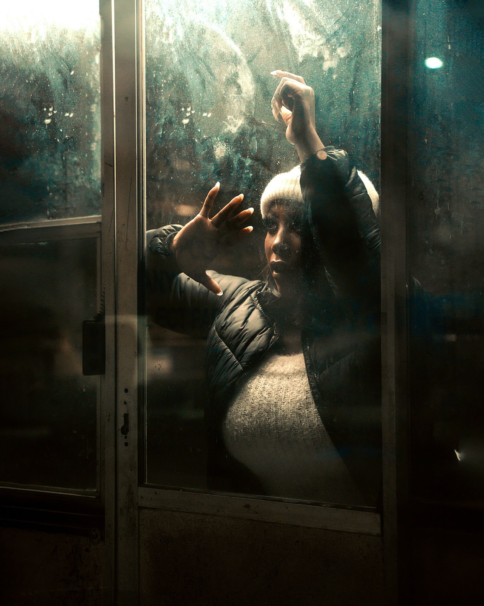 Child taking a selfie through a foggy window, with hand raised and reflection visible.