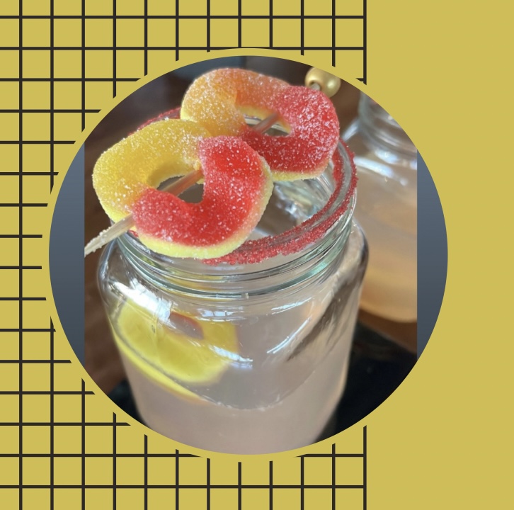Gummy candies on a stick above a glass jar with lemon slices, against a yellow and black grid background.