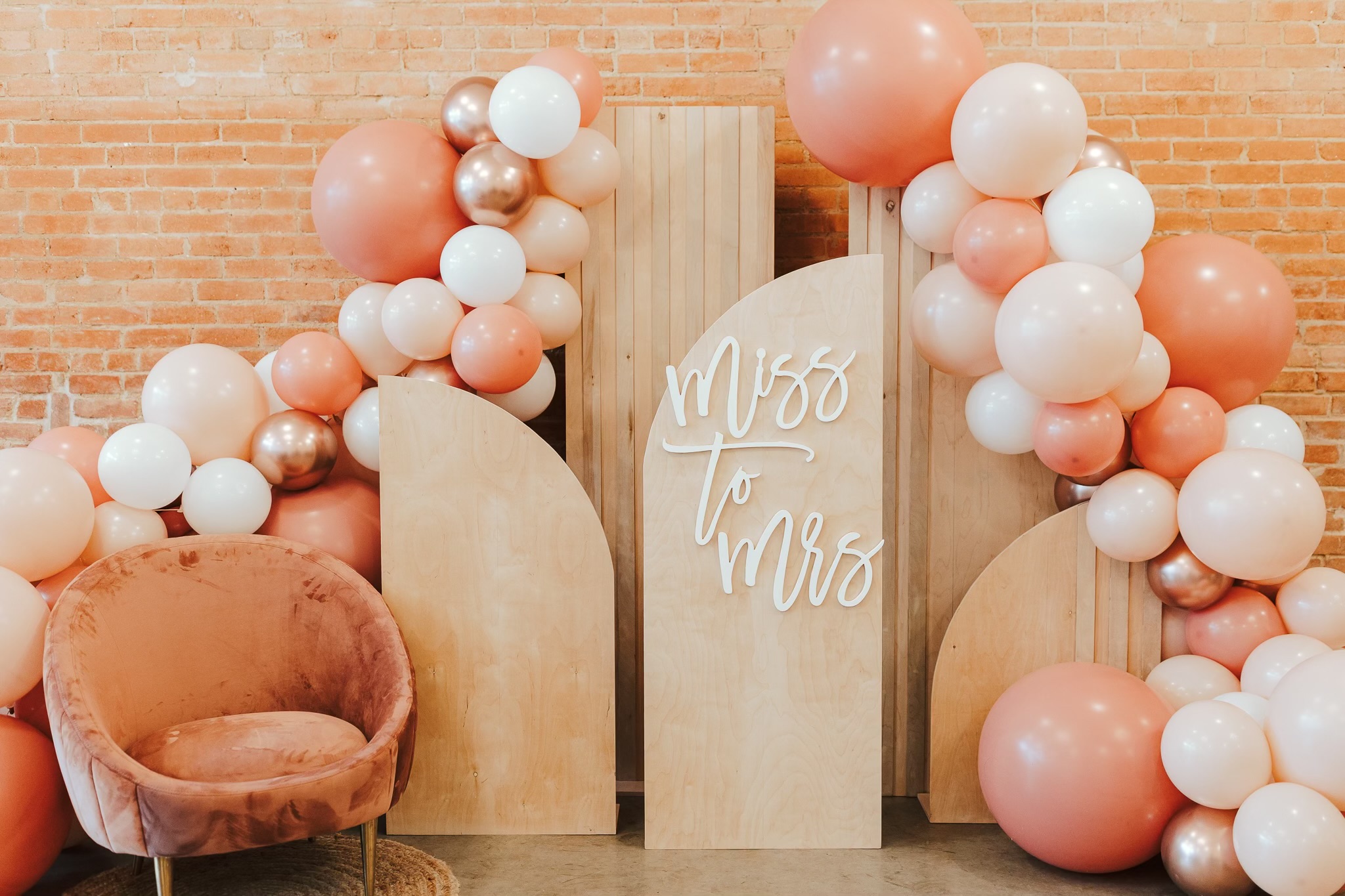 Decorative setup with balloons and a sign reading 'Miss to Mrs' on a brick wall background.