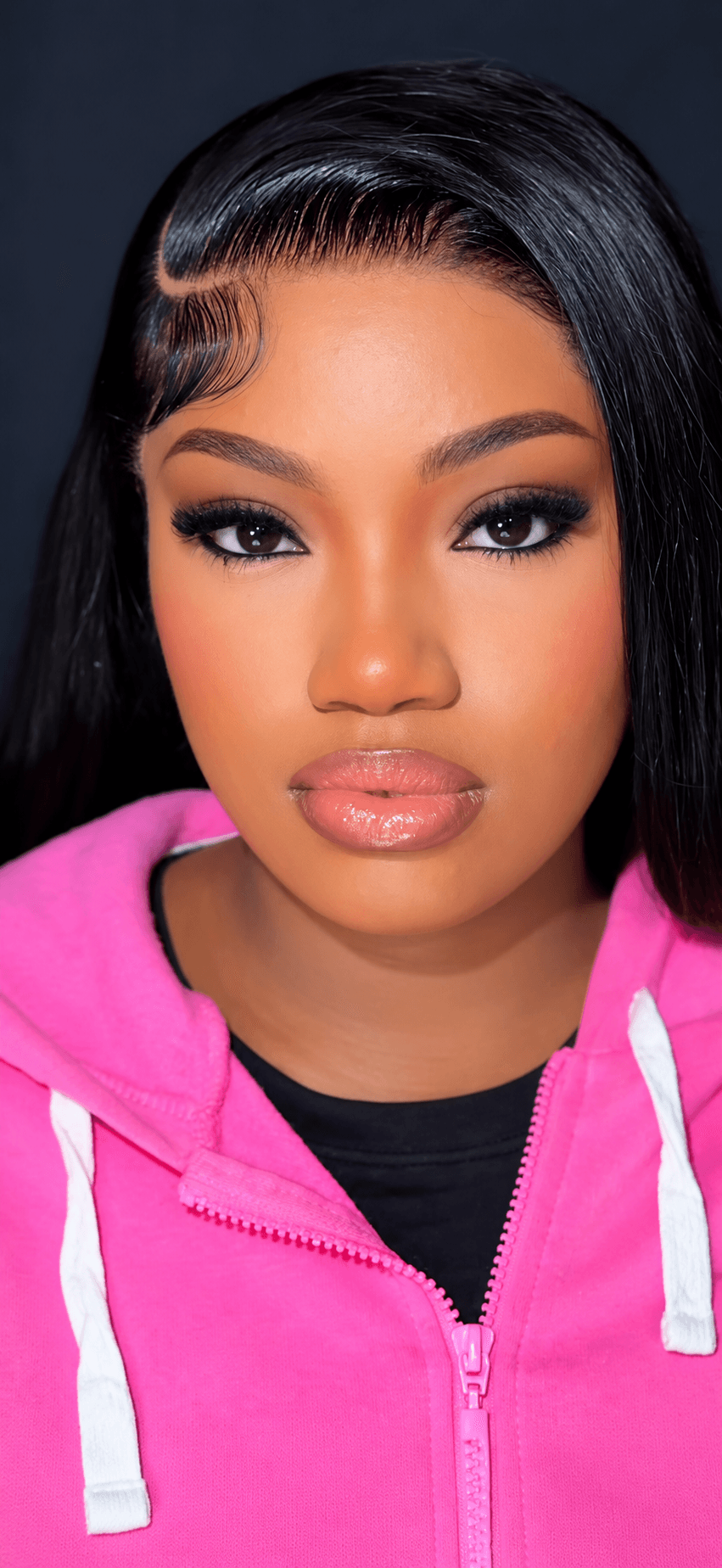 Close-up of a woman with dark hair, makeup, and a pink hoodie, facing forward.