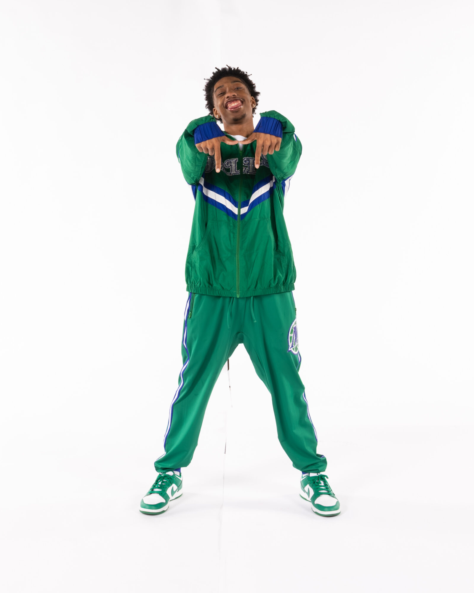 Young man in green sportswear smiling and pointing forward, standing against a white background.