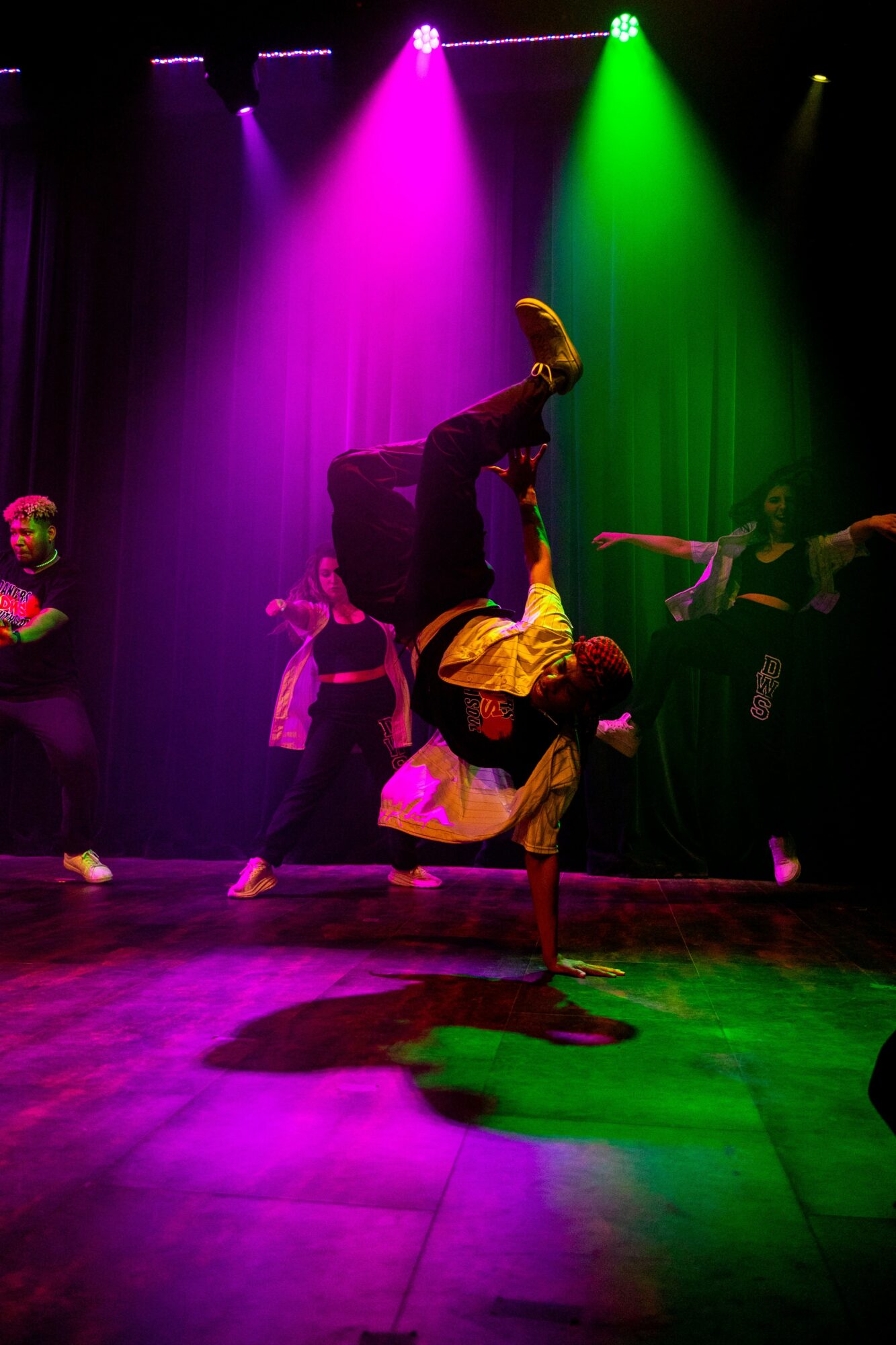 Performer in a yellow and black costume doing a handstand on stage with colorful lighting.