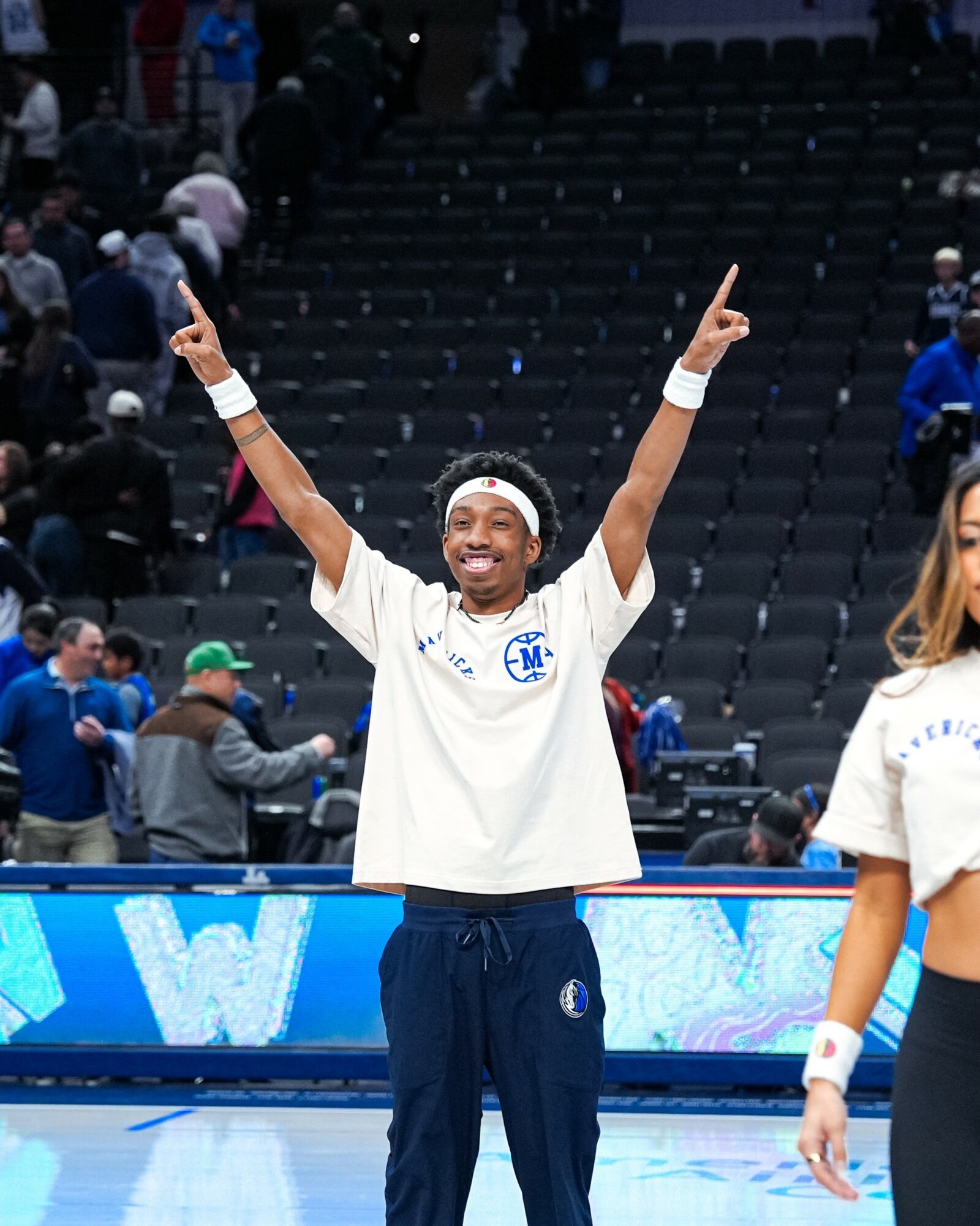 Tennis player celebrating with arms raised, smiling, in a sports arena with spectators in the background.