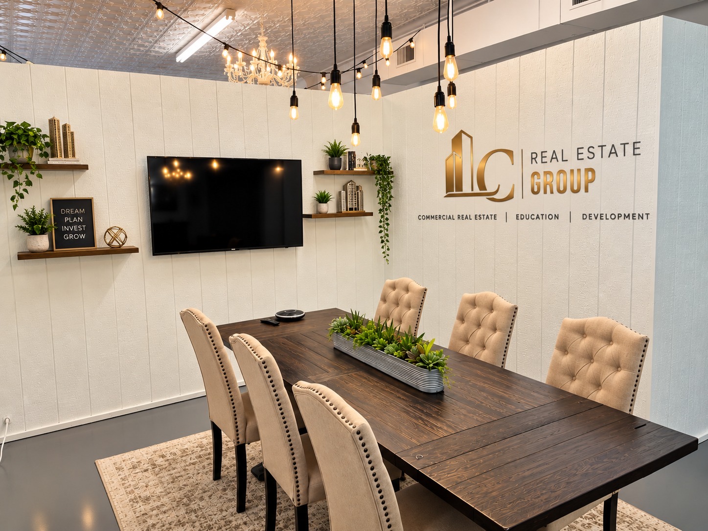 Modern office conference room with a long wooden table, six beige tufted chairs, a wall-mounted TV, and a logo on the wall.