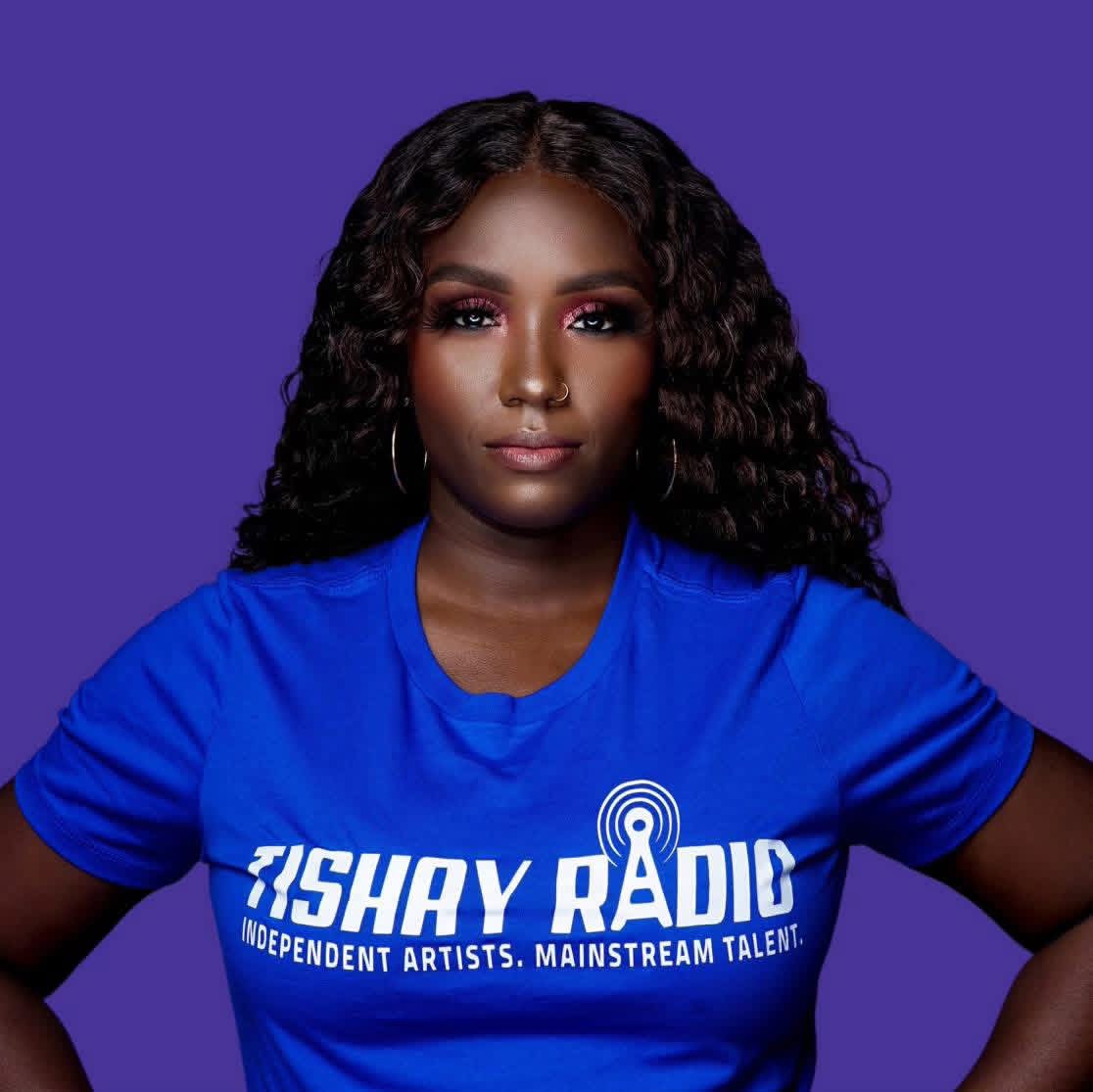 Woman with curly hair wearing a blue T-shirt with radio station logo against purple background.
