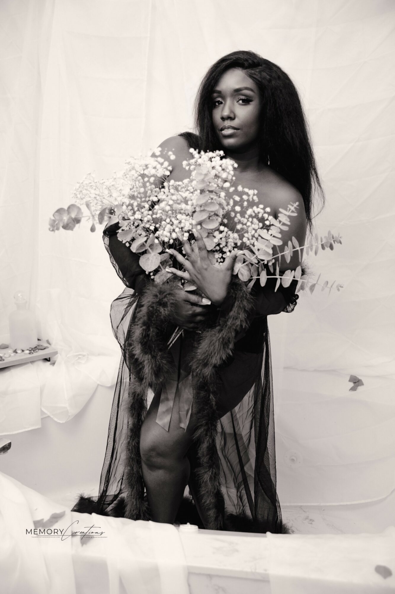 Woman holding a large bouquet of flowers, wearing a sheer dress, standing against a plain background.