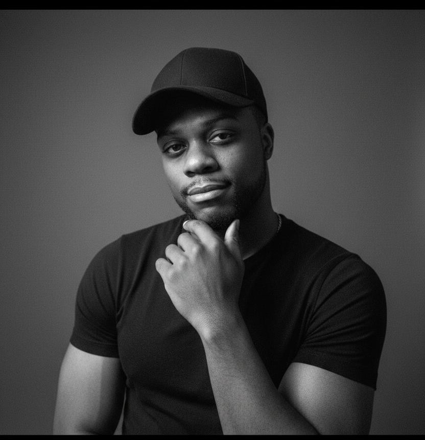 Young man wearing a cap and black t-shirt, resting his chin on his hand, looking at the camera, neutral expression.