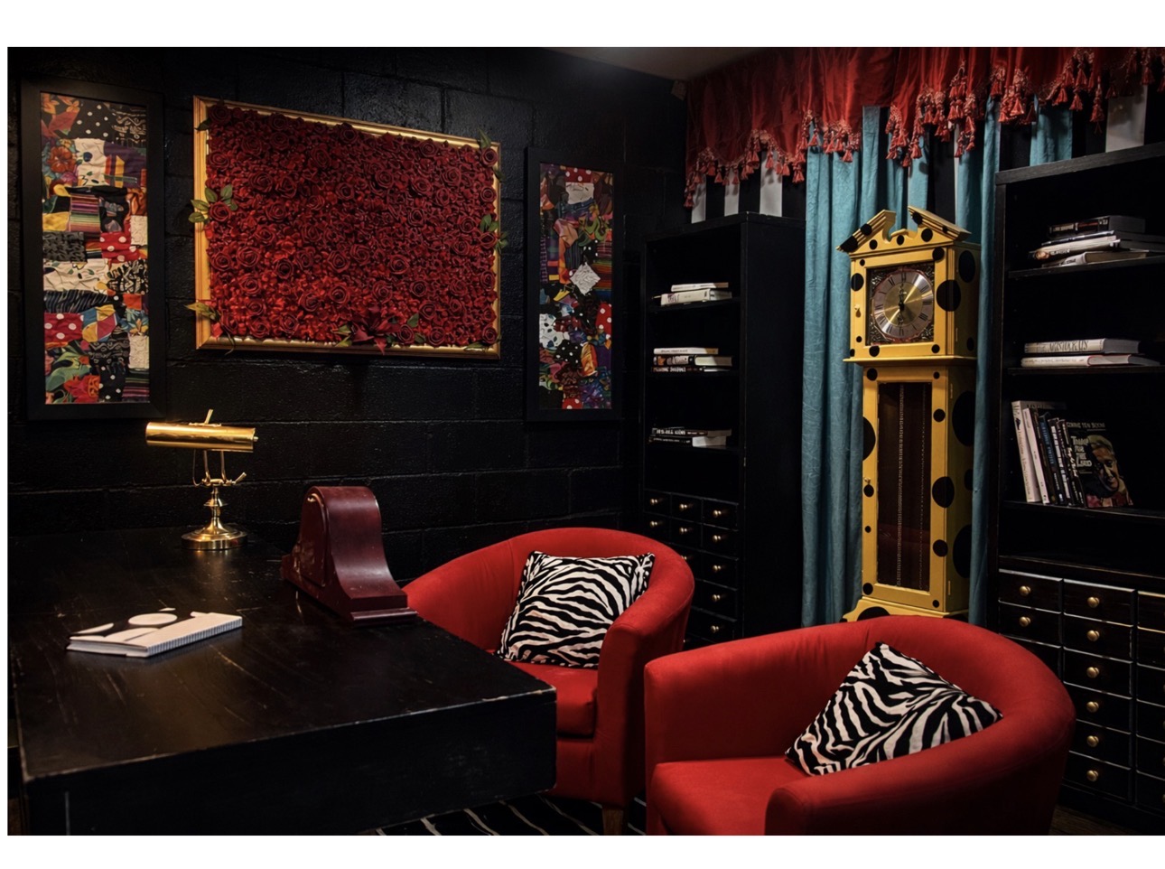 Room with dark walls, red curtains, black bookshelves, yellow clock, and red chairs with zebra-patterned pillows.