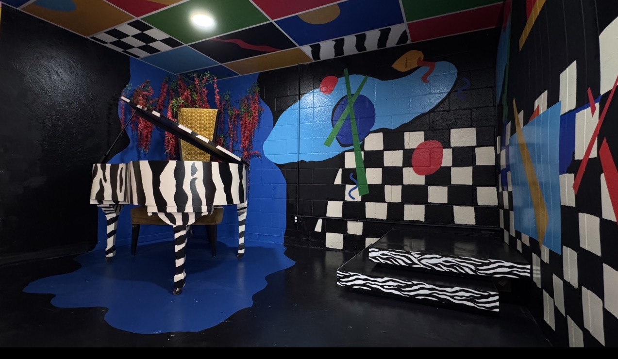 Room with colorful abstract murals, zebra patterns, and a black-and-white checkered wall, featuring a zebra-striped table and a black-and-white striped bench.