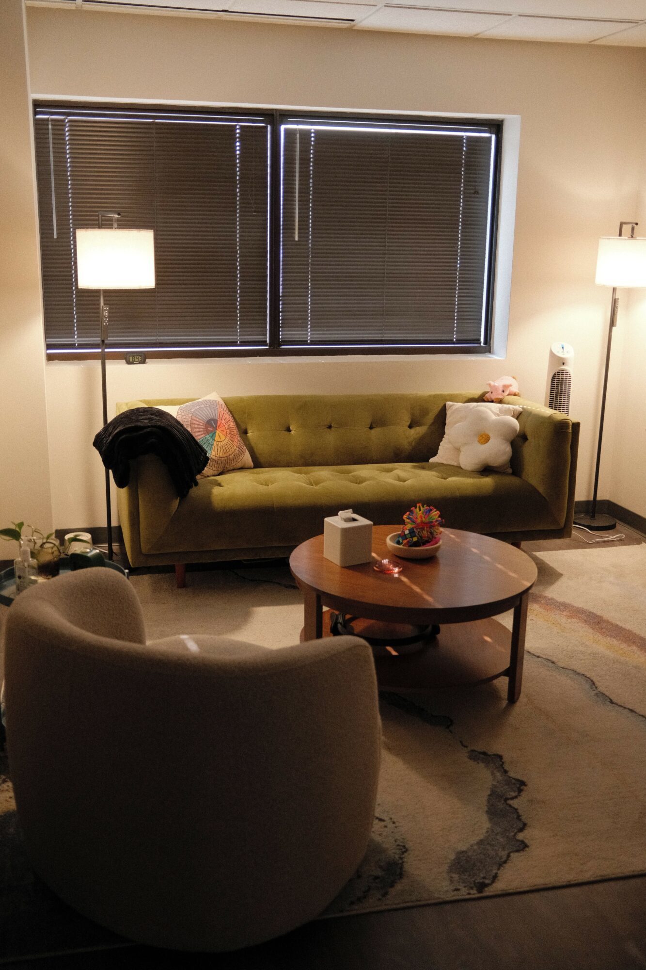 Living room with green sofa, round coffee table, and window with blinds, viewed from the side.