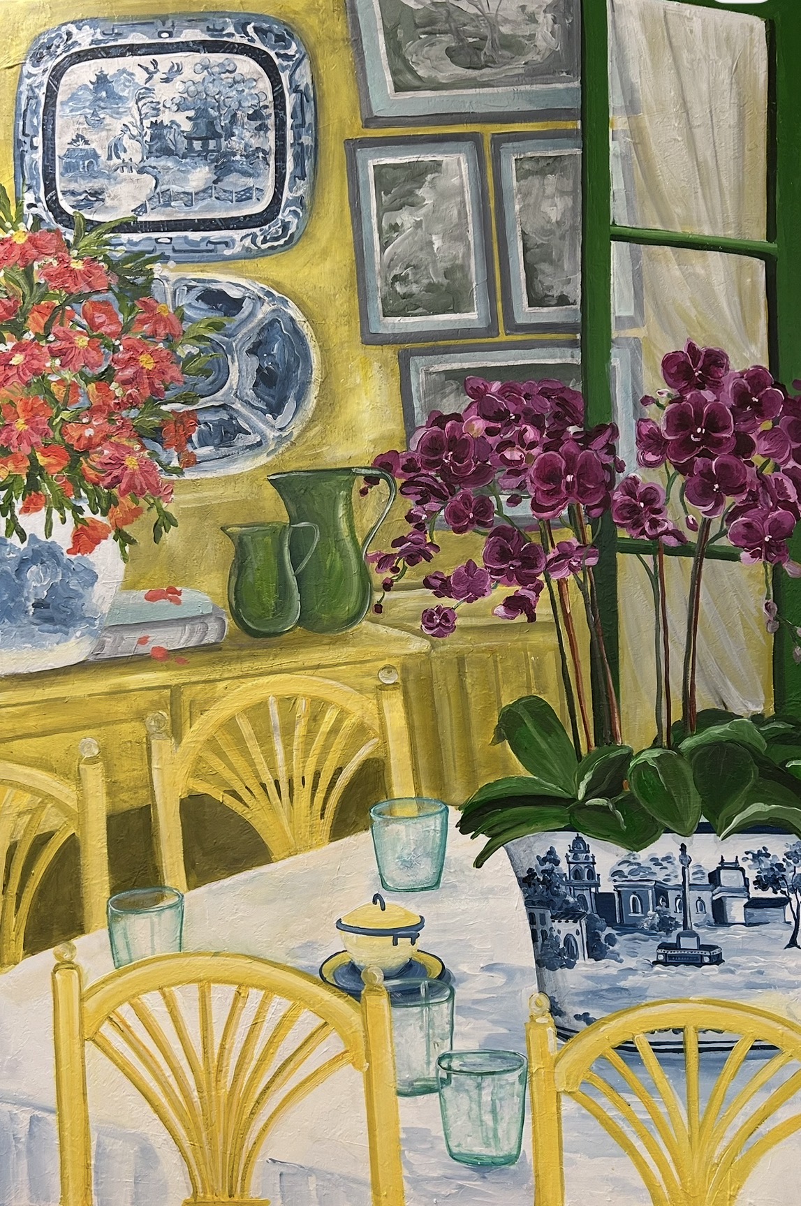 Interior scene with yellow furniture, purple orchids, framed artwork, and a window with green trim.