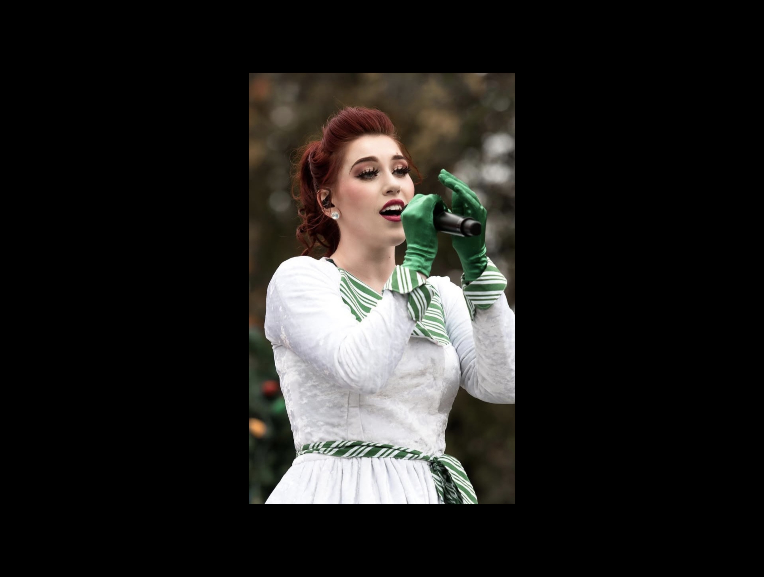 Woman with red hair wearing a white dress with green accents, holding a green telephone outdoors.
