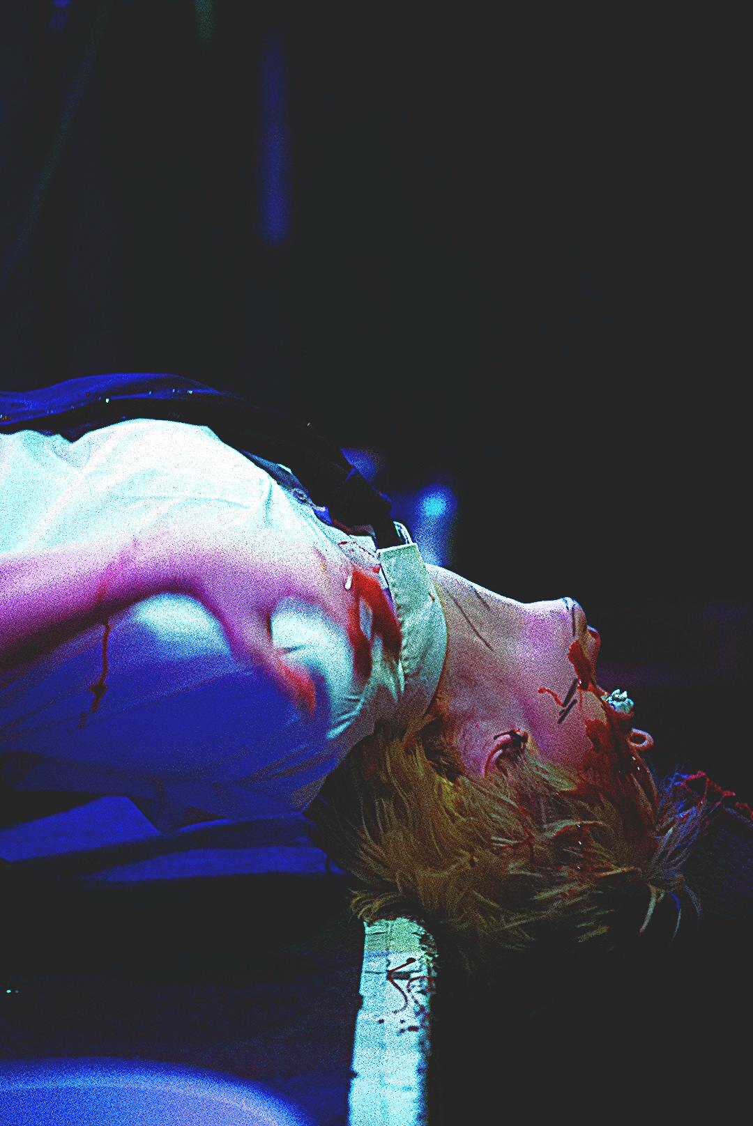 Person lying on the ground with blood on face and head injuries, in a dark environment.
