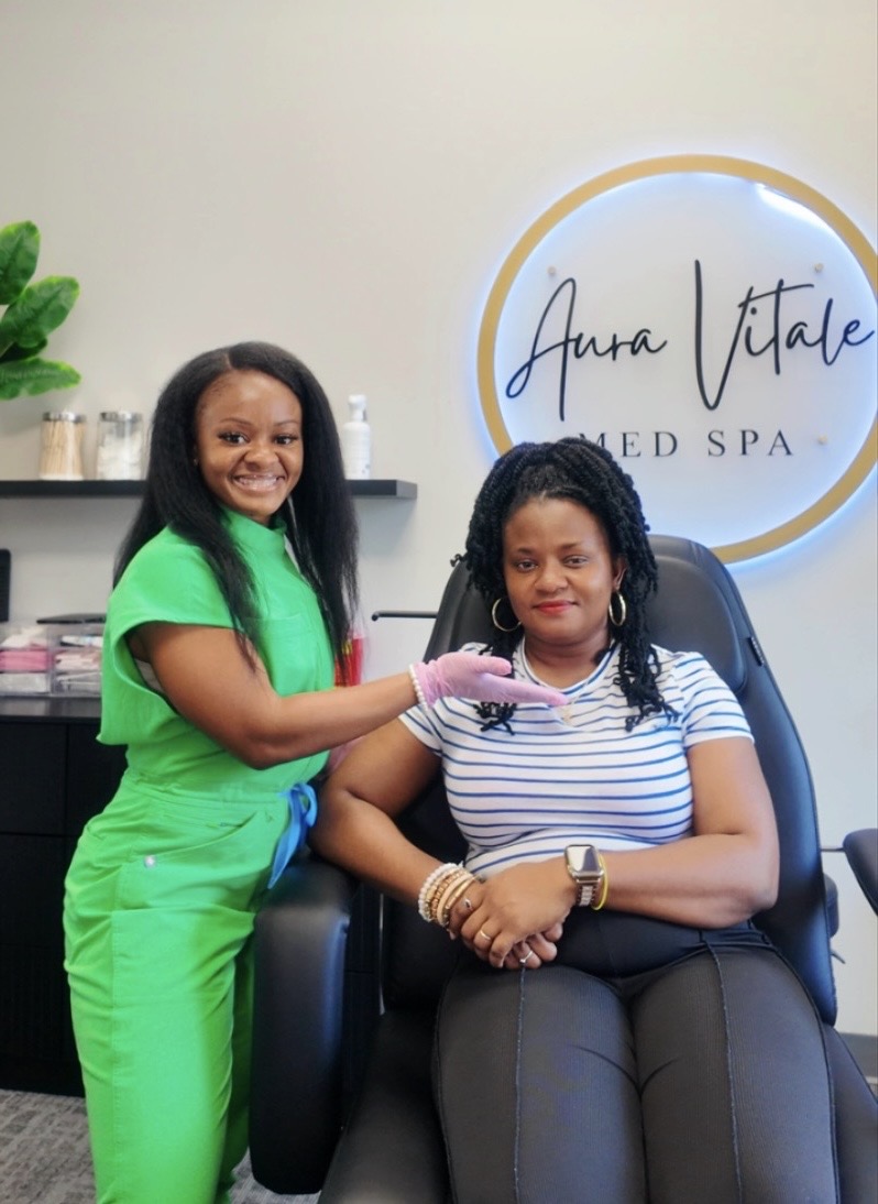 Two women in a spa, one standing and smiling, the other sitting in a chair, with a spa sign in the background.