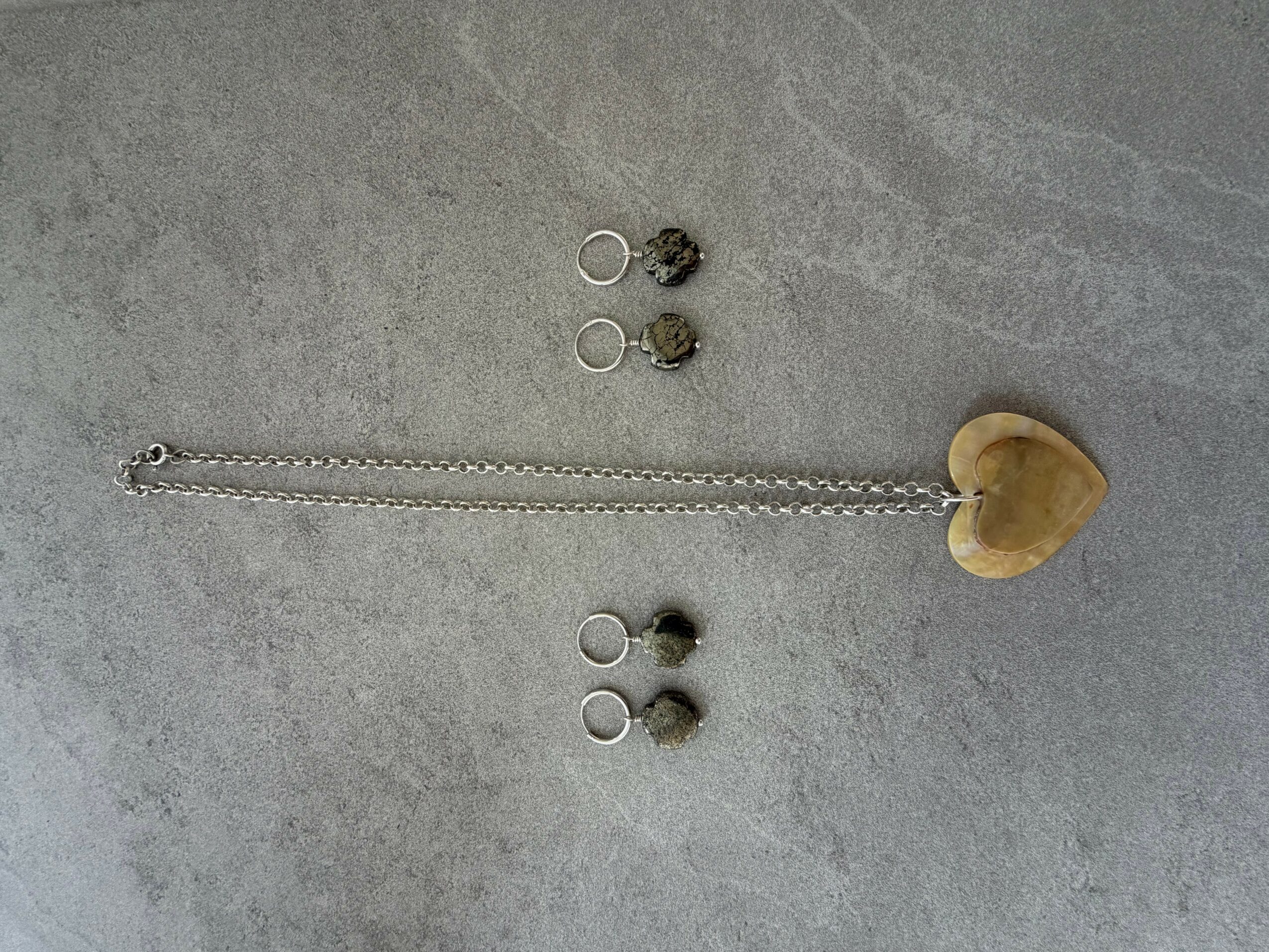 Jewelry pieces including earrings, a chain, and a heart-shaped pendant on a gray surface.