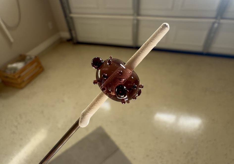 Chocolate-covered ladybug-shaped treat on a stick held in a room with a beige carpet and a closed garage door