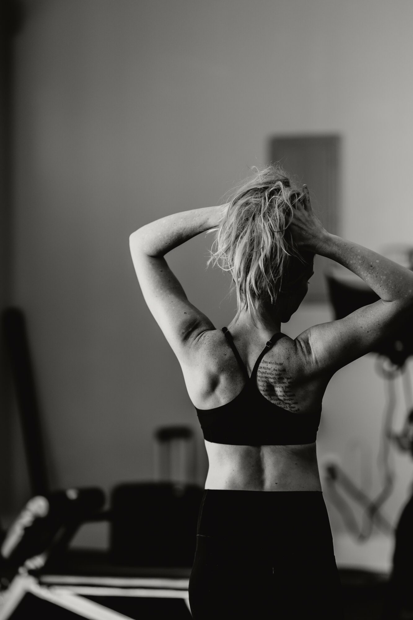 Woman with short hair adjusting her hair in front of a mirror, back view, black and white.