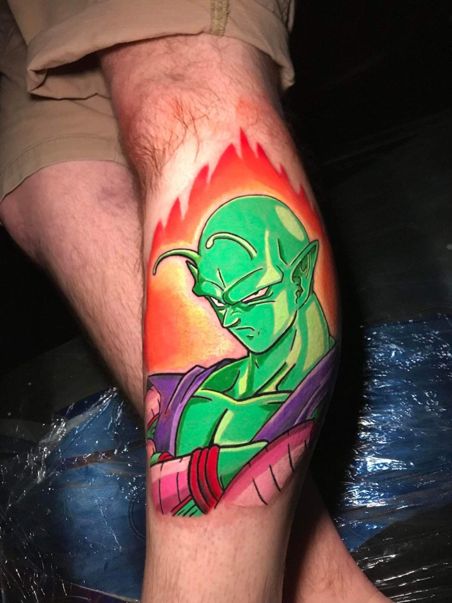 Tattoo of a green character with pointed ears and a serious expression, surrounded by flames, on a person's leg.