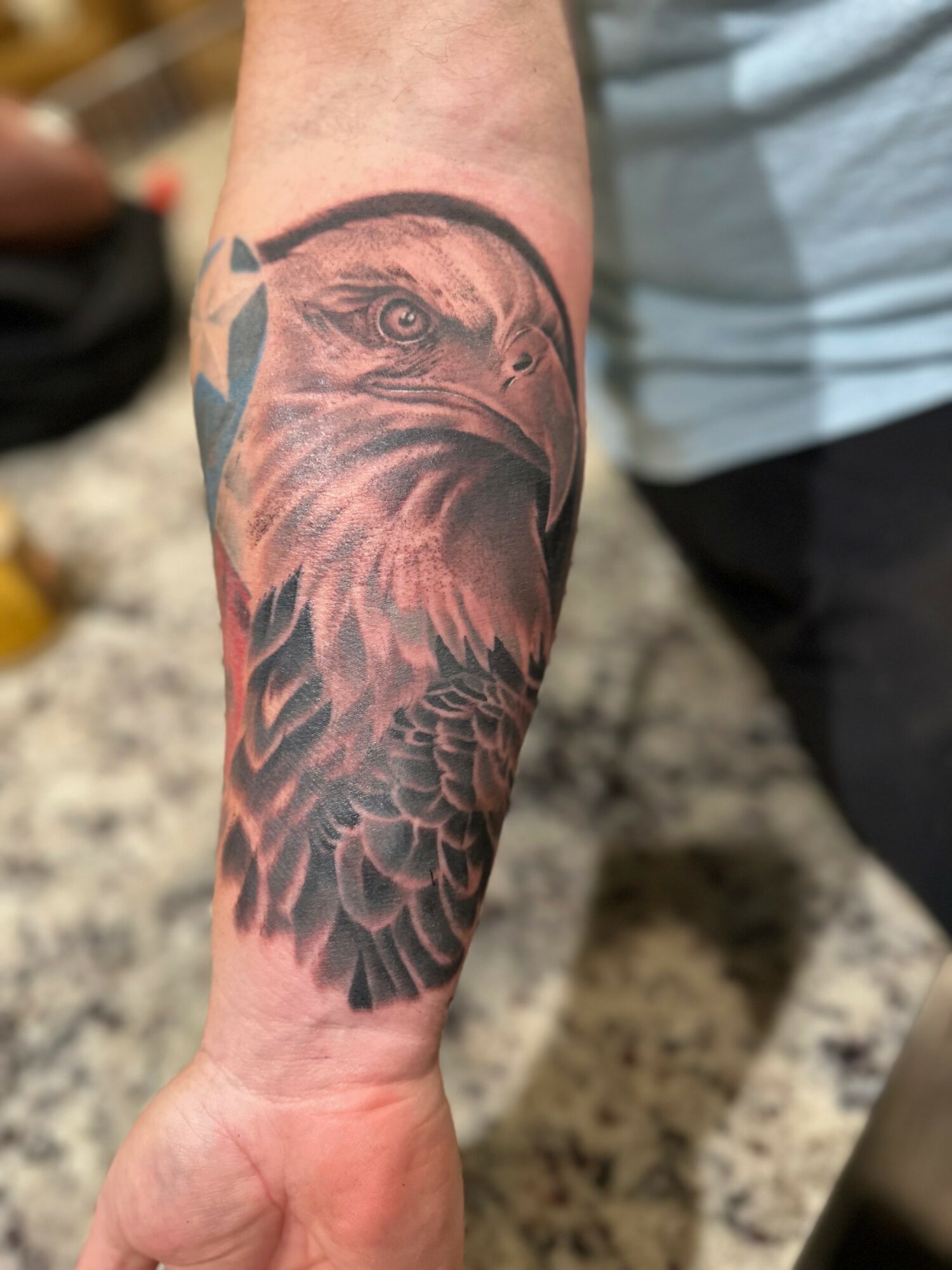 Tattoo of an eagle's head and feathers on a person's forearm, detailed and shaded in black and gray.