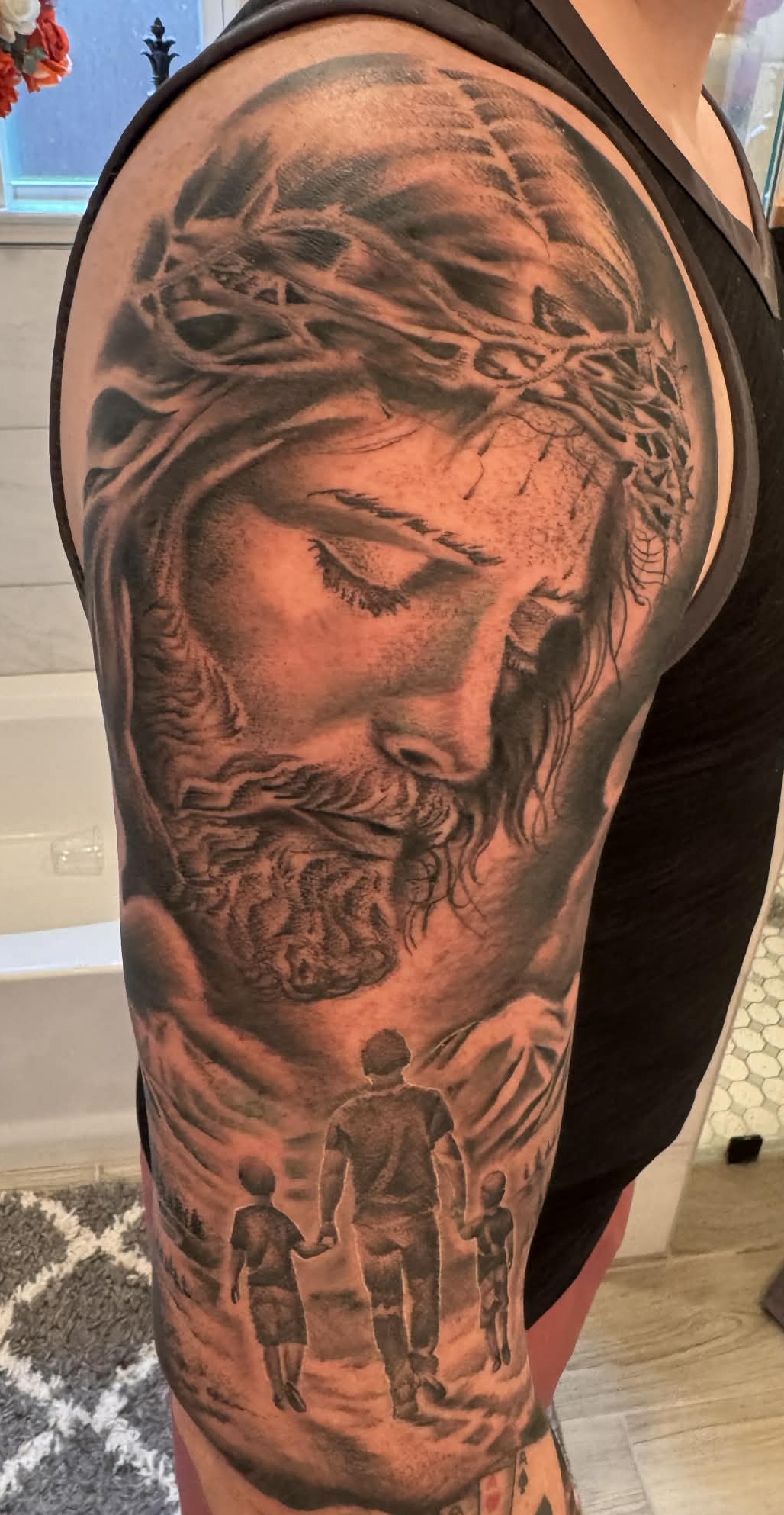 Tattoo of Jesus Christ with a crown of thorns, two children holding hands, and a landscape scene, all in black and gray.