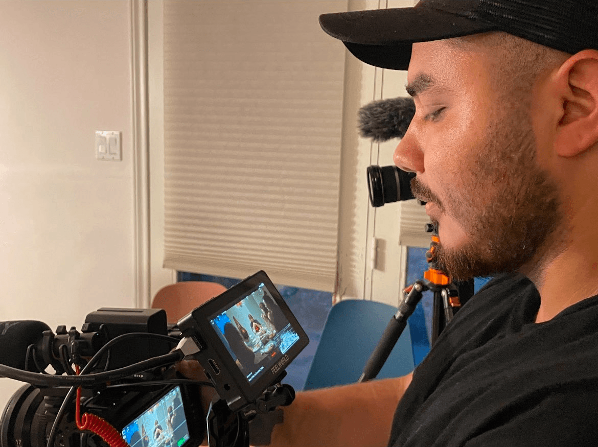 Man operating a camera with a monitor, focusing on the screen, in an indoor setting.