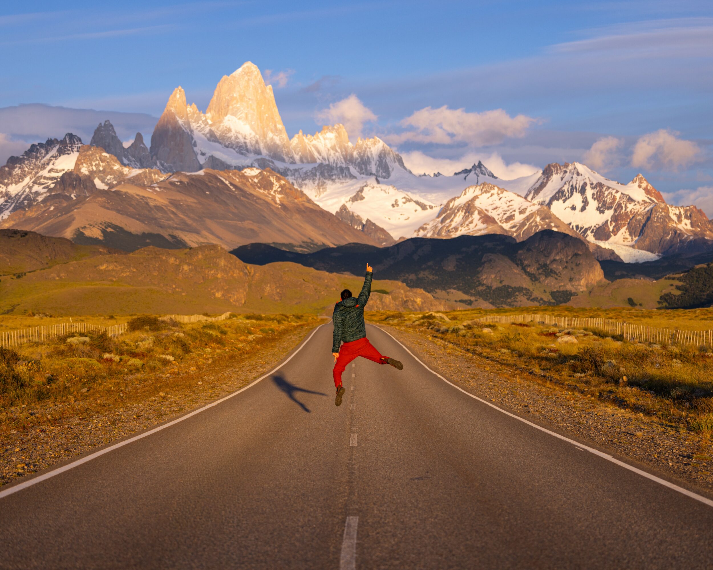 Person jumping in the middle of a road with mountains and sky in the background.