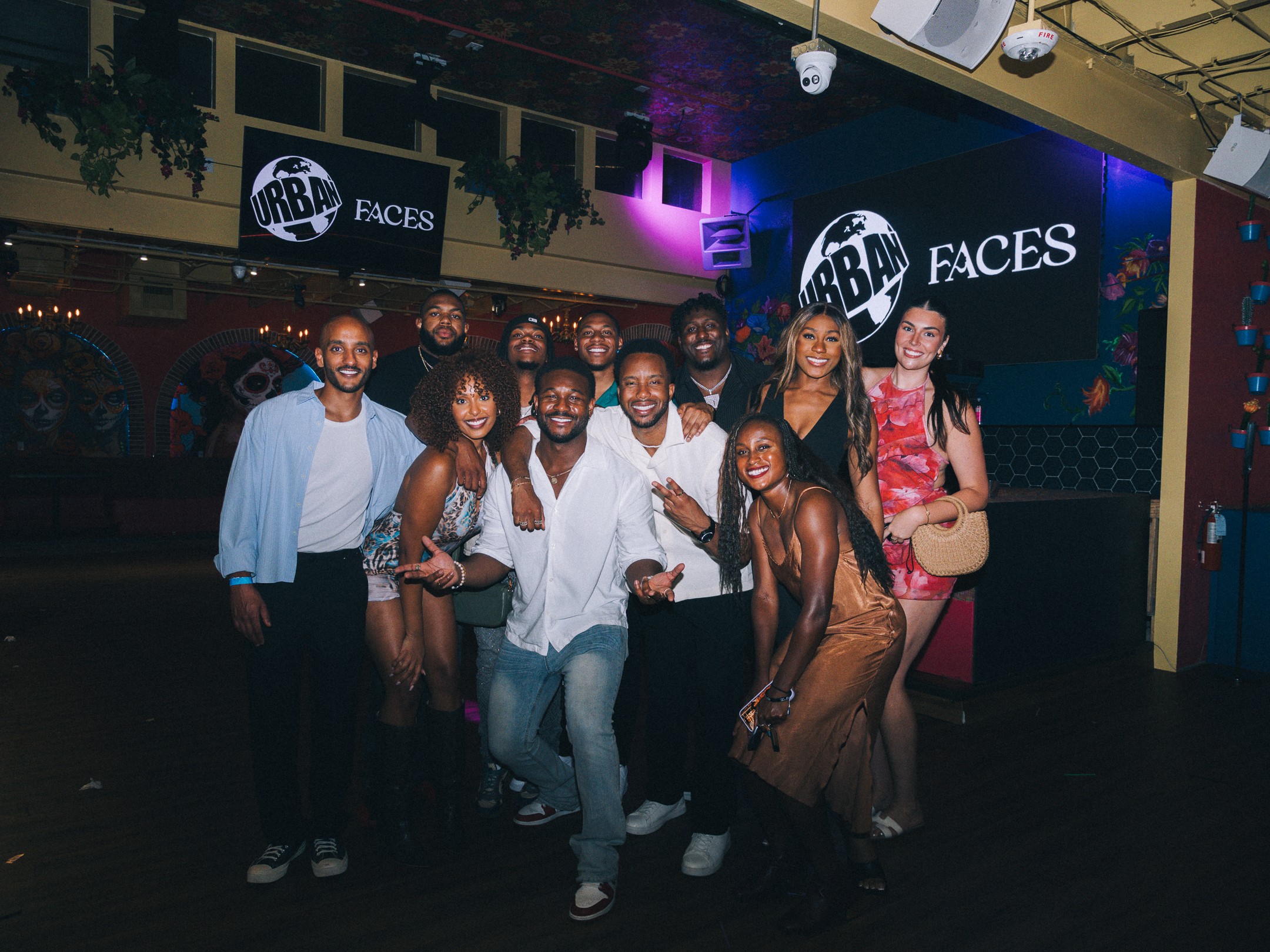 Group of nine people smiling and posing in a nightclub with colorful lights and ARBAFACES signs.