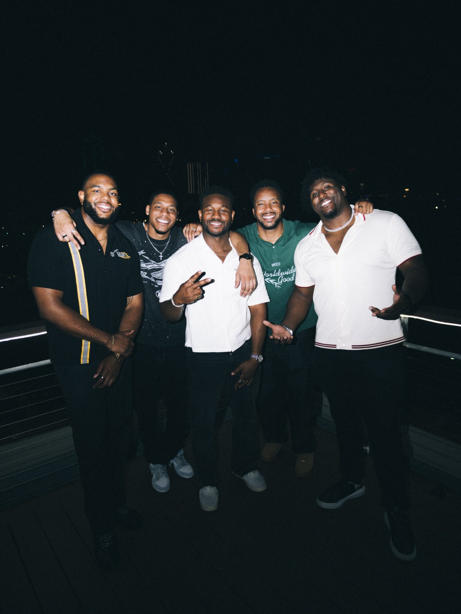 Group of six men standing together outdoors at night, smiling and posing for the photo.