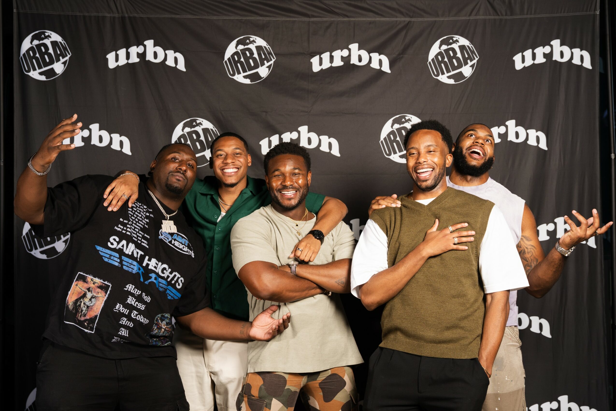 Group of five smiling people standing in front of a black backdrop with white 'urban' logos, posing happily.