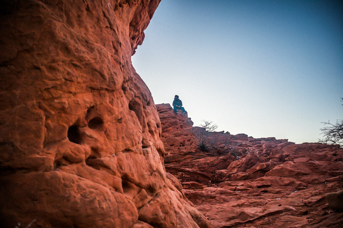 Person sitting on a rocky hilltop with a clear sky background.