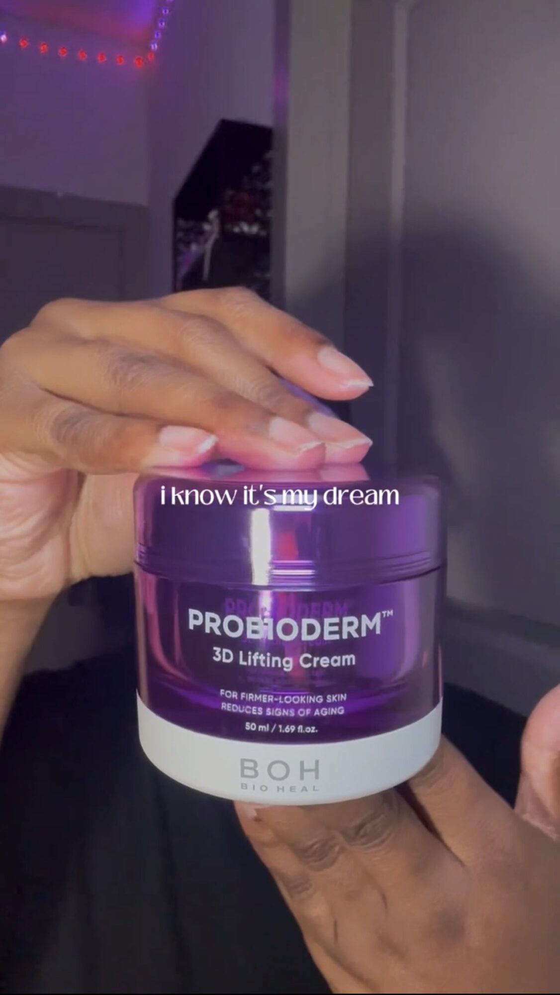 Person holding a purple jar of Probioderm 3D Lifting Cream with text on the jar, in a room with purple lighting.