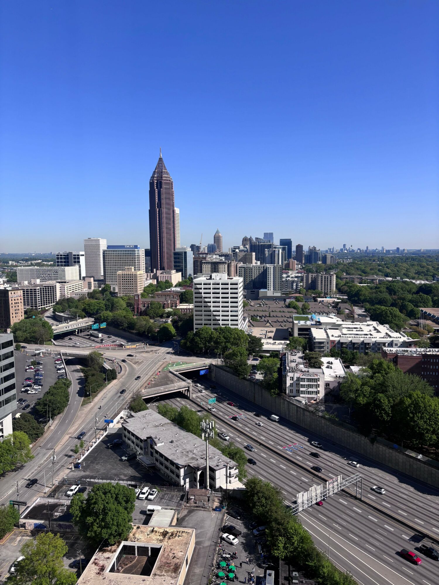 City skyline with tall buildings, roads, and greenery under a clear blue sky.