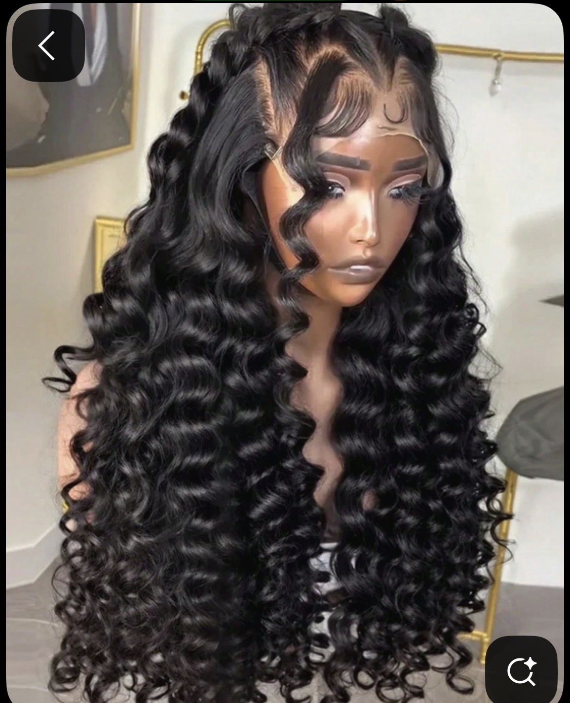 Young woman with long, curly hair styled in defined ringlets, wearing makeup, in a room with a mirror and clothing rack.